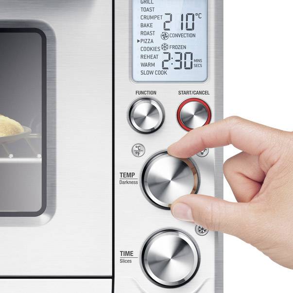 Ręka obraca pokrętłem ustawień na piecu, który jest ustawiony na grillowanie w temperaturze 210°C. Wyświetlacz pokazuje timer i funkcje.