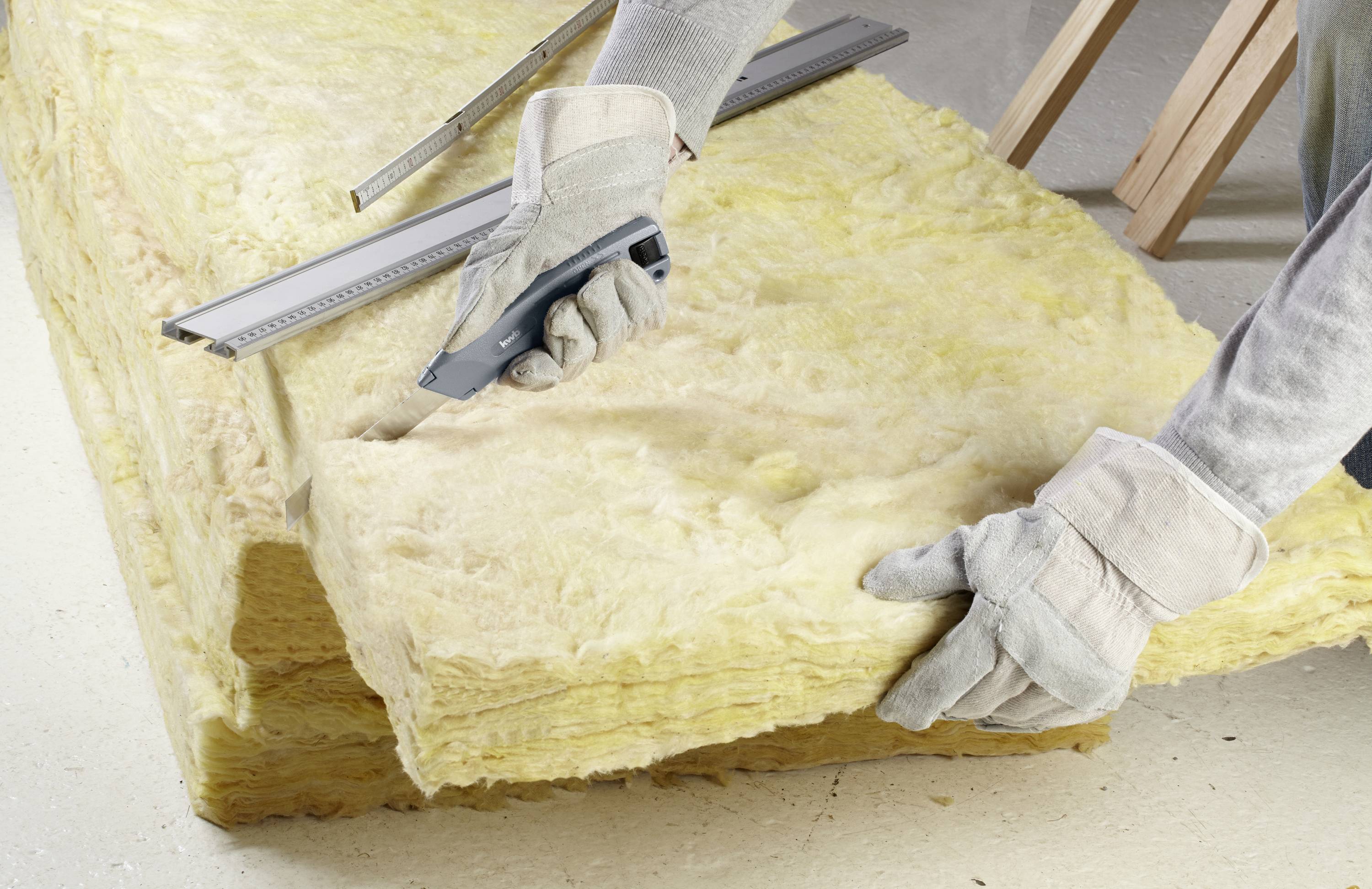 Osoba wycina nożem płytę z żółtej wełny szklanej. Używana jest odzież ochronna.