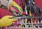 Pracownik w żółtych rękawicach zdejmuje izolację z grubego kabla za pomocą specjalnego czerwonego noża. W tle widoczne są kolejne kable.