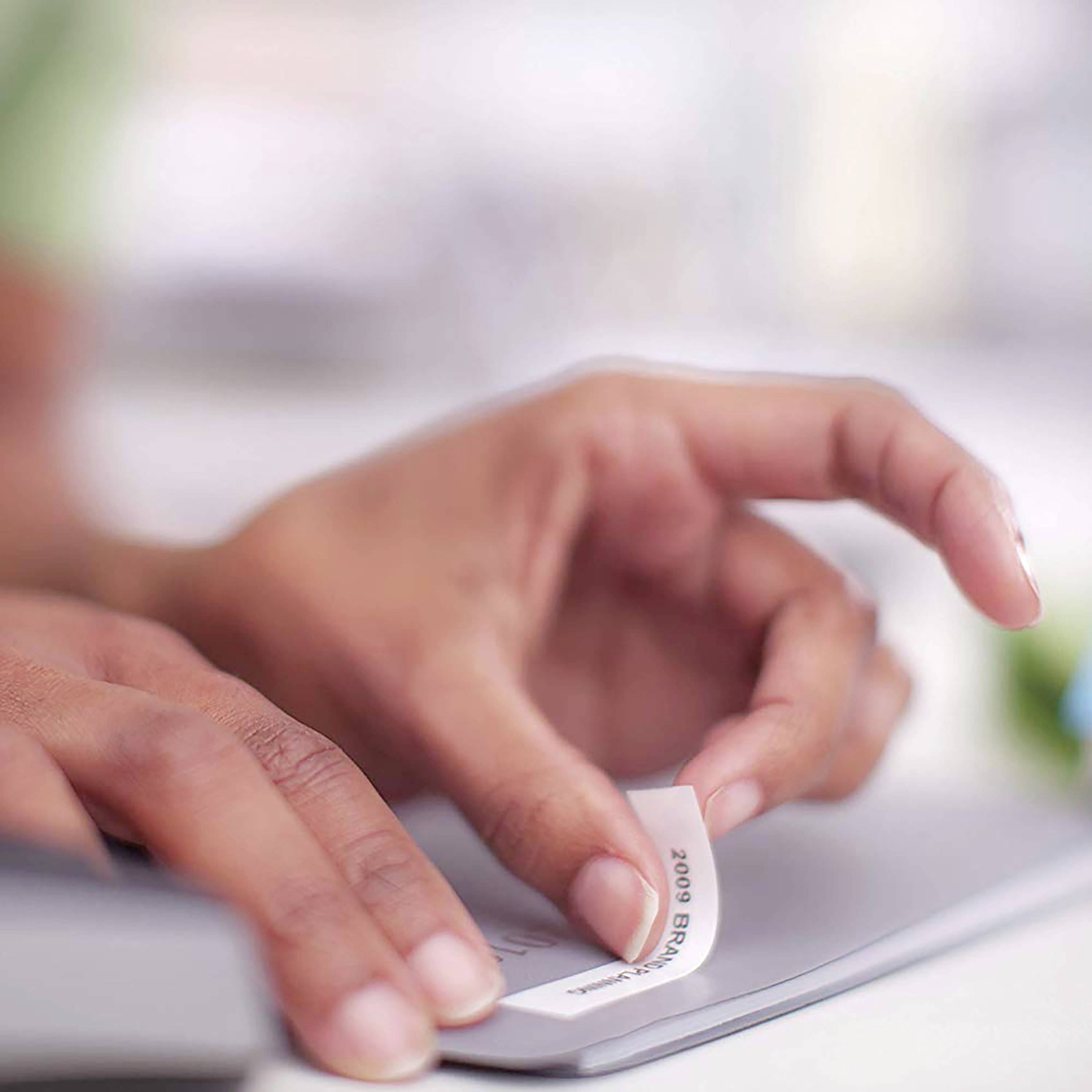 Dłoń wkłada białą serwetką czyszczącą do urządzenia elektronicznego, aby je wyczyścić. Nacisk kładziony jest na czystość i higienę.