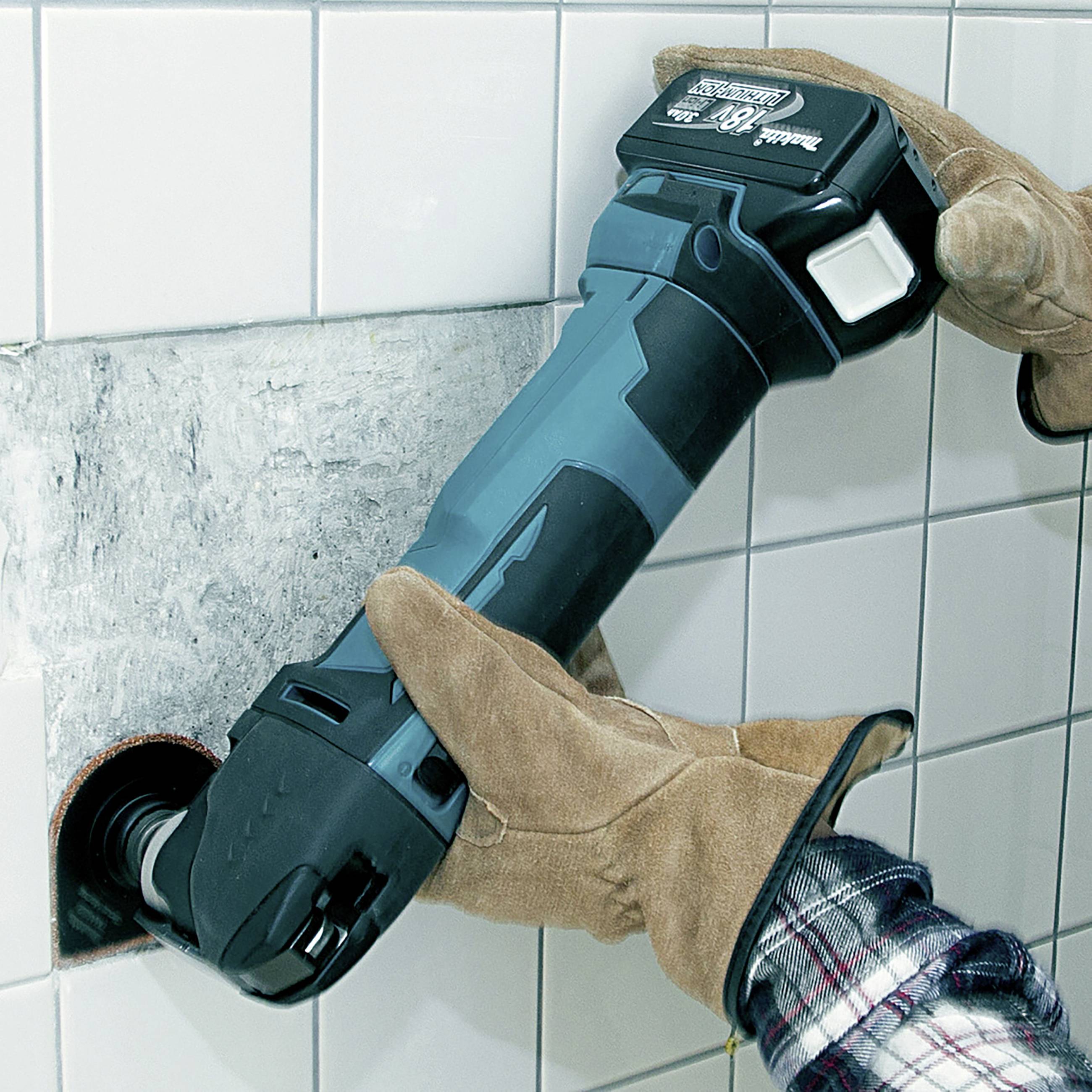 Osoba w rękawiczkach używa elektronarzędzia do cięcia płytki w ścianie.