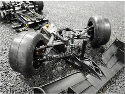 Zbliżenie zdalnie sterowanego samochodu wyścigowego na asfaltowym torze. Szczegółowy widok przedniej części podwozia i opon.