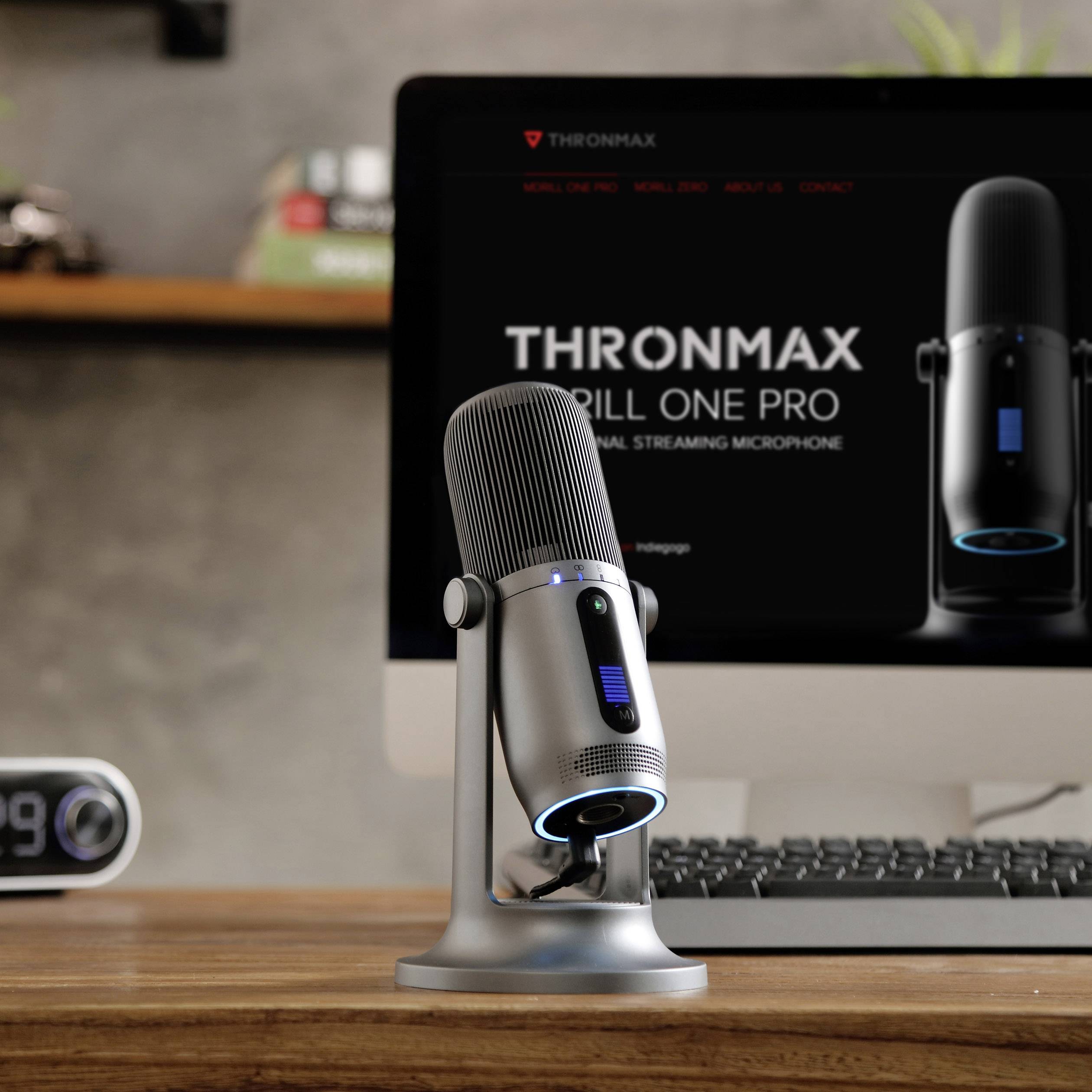 Nowoczesny mikrofon na biurku przed ekranem komputera wyświetlającym reklamę tego samego modelu mikrofonu.