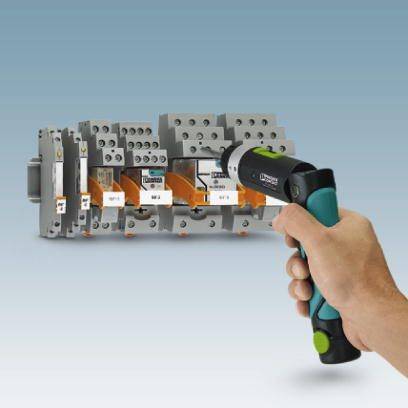 Jedna ręka trzyma termometr na podczerwień skierowany na rząd elektrycznych przełączników zainstalowanych w szafce sterowniczej.