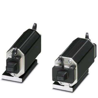 Dwa czarne obudowy z tworzywa sztucznego z podłączeniami kablowymi, zamontowane na metalowych wspornikach. Wyglądają jak elementy elektryczne.