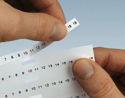 Dwie ręce odrywają ponumerowane paski etykiet z numerami od 7 do 18.