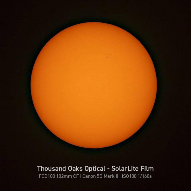Pomarańczowa tarcza słoneczna na czarnym tle, z małą plamą słoneczną. Tekst: 'Thousand Oaks Optical - SolarLite Film'.