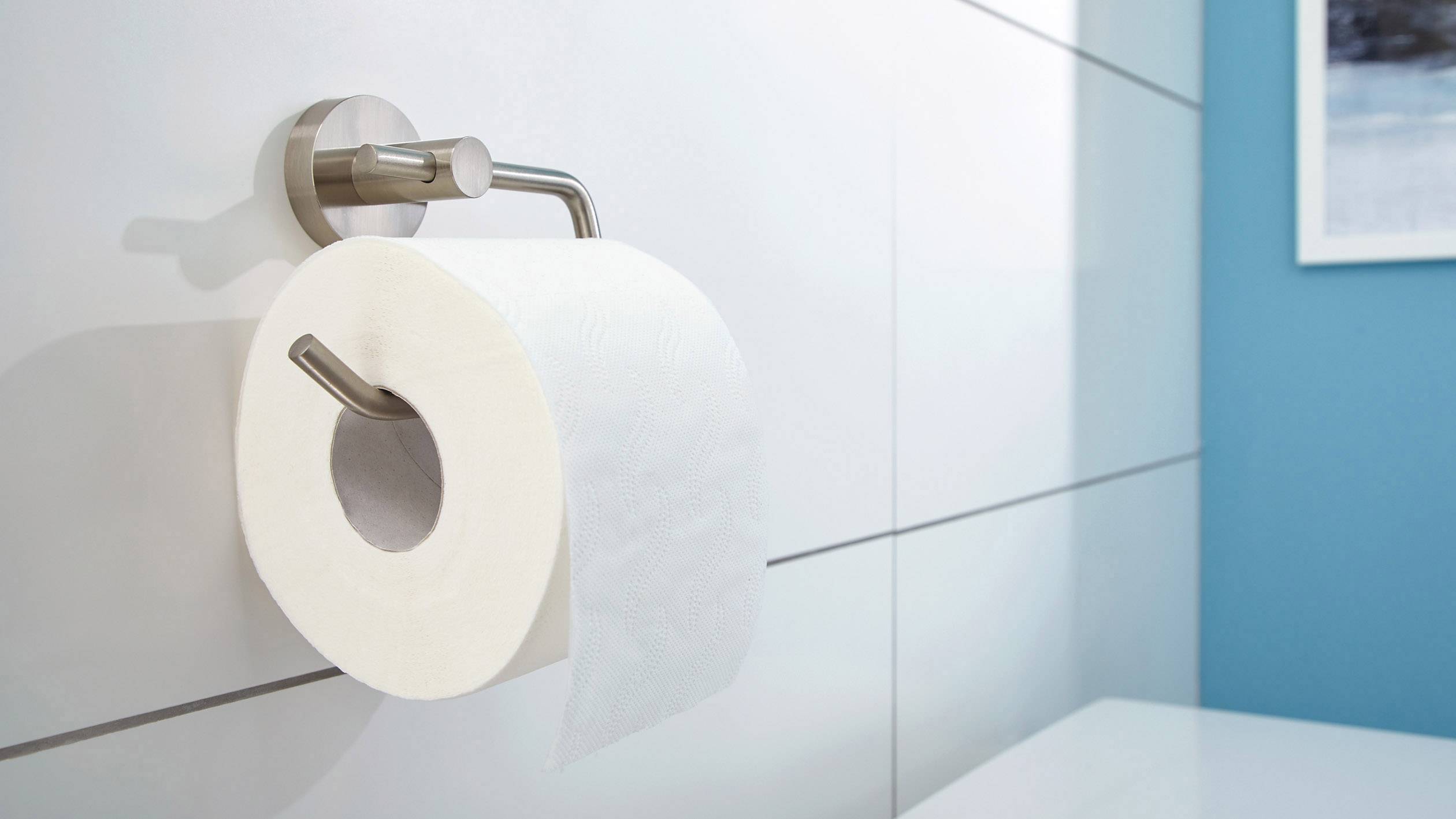 Rolka papieru toaletowego na uchwycie ściennym w nowocześnie urządzonym łazience z białymi płytkami ceramicznymi i niebieską ścianą.