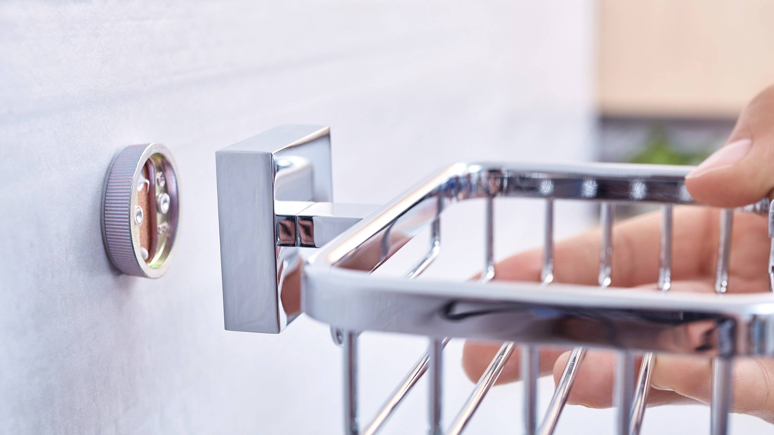 Dłoń mocuje prostokątną metalową półkę prysznicową na ścianie za pomocą przyssawki.