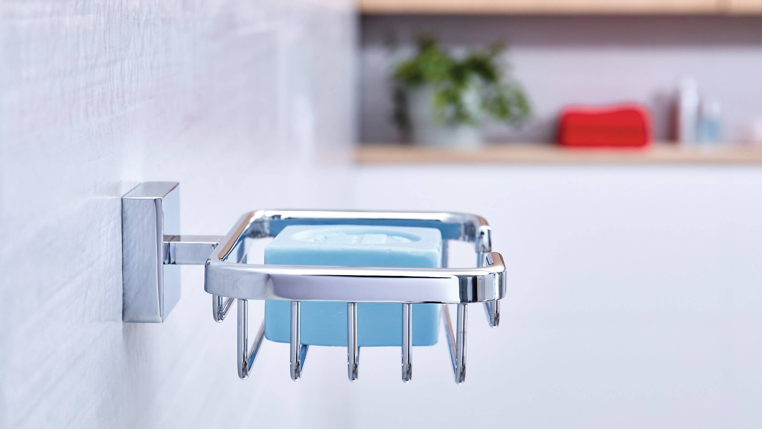 Niebieskie mydło leży w nowoczesnym, chromowanym uchwycie na białej ścianie łazienki. W tle rozmyte.