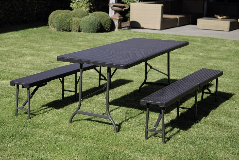 Prostokątny stół z dwoma ławkami stoi na zielonym trawniku przed nowoczesną przestrzenią zewnętrzną, otoczoną żywopłotem i wyposażoną w meble.