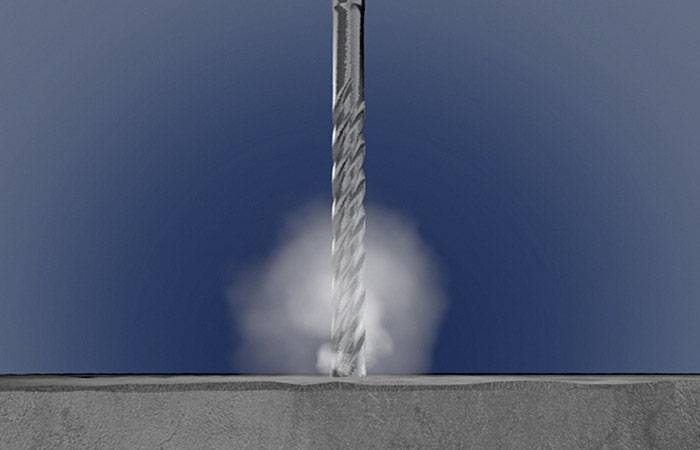 Wiertło przenika beton, tworząc obłoki pyłu.