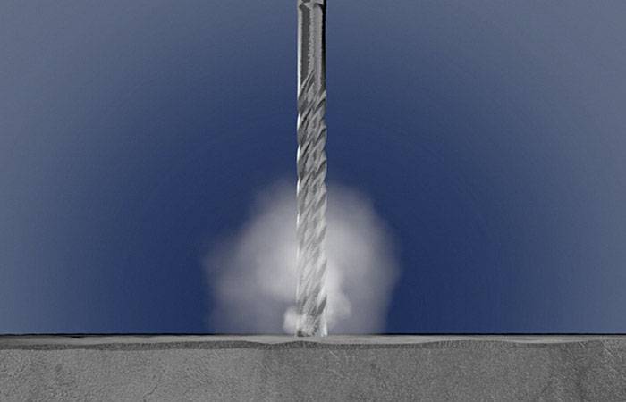 Wiertło przebija powierzchnię betonową, wytwarzając pył i prezentując proces wiercenia w akcji.