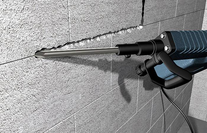 Niebieski elektryczny młot udarowy jest używany do wycinania prostej linii w szarej ścianie betonowej.