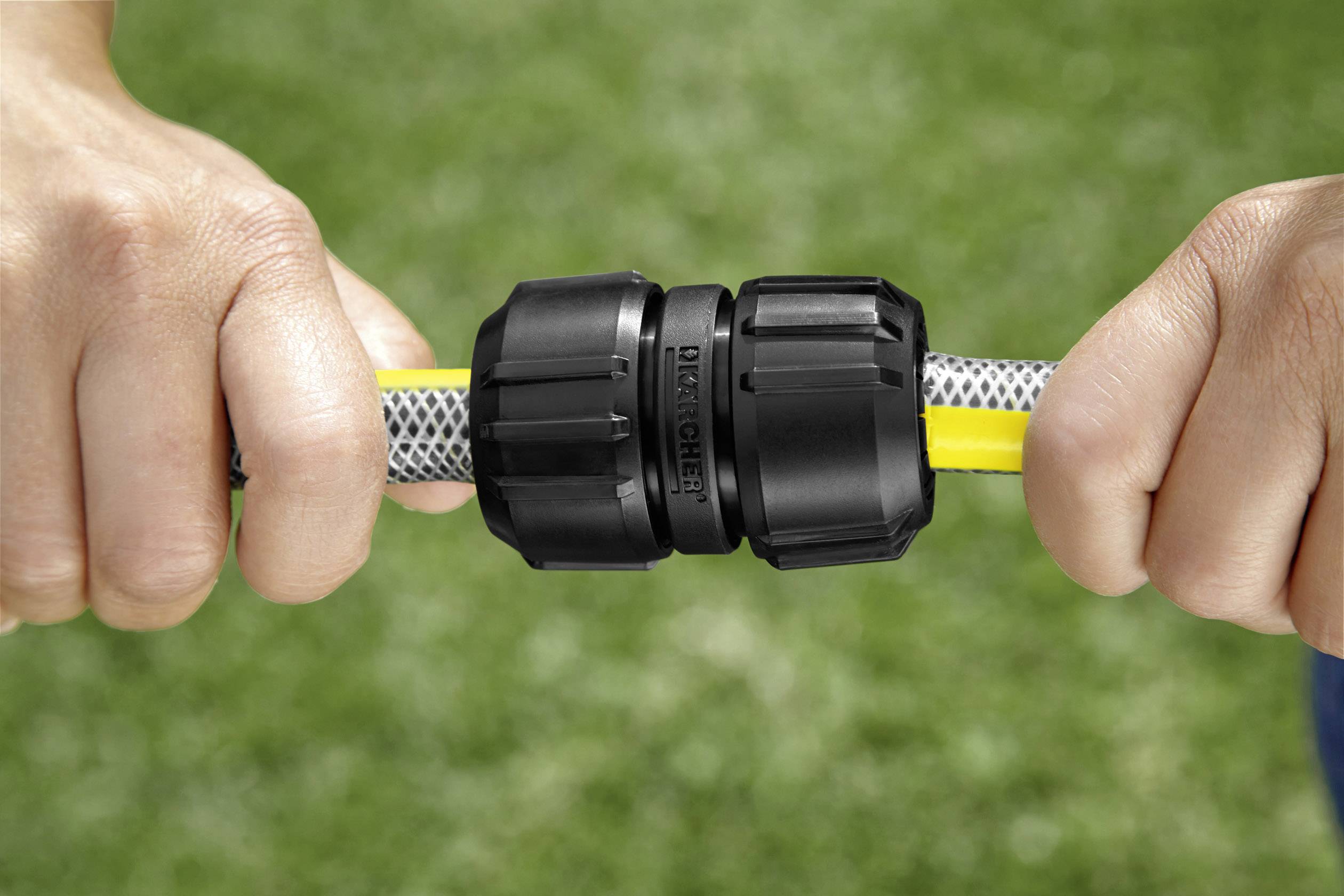 Ręce łączą dwa przewody czarnym szybkozłączem. W tle widać trawę.