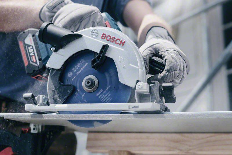 Rzemieślnik przecina deskę piłą ręczną Bosch. Nosi rękawice i precyzyjnie pracuje nad projektem.