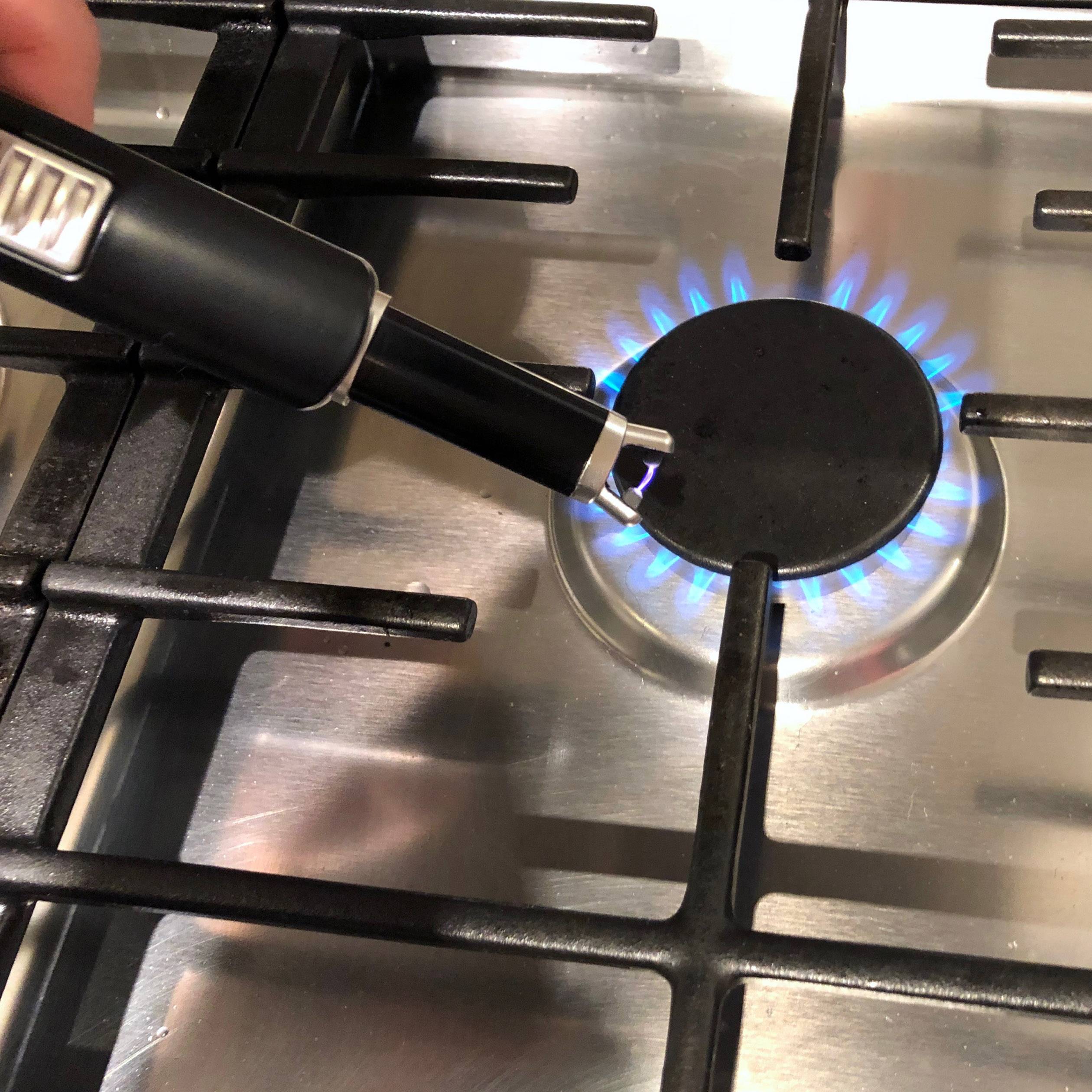 Kuchenka gazowa jest zapalana za pomocą zapalniczki. Niebieski płomień płonie pod jednym z palników na kuchence.