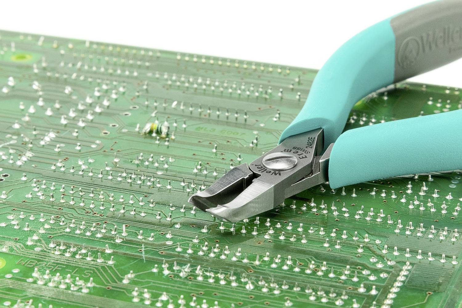 Zielona płytka drukowana z widocznymi obwodami elektronicznymi, na której spoczywa zielono-niebieskie szczypce przeznaczone do prac elektronicznych.