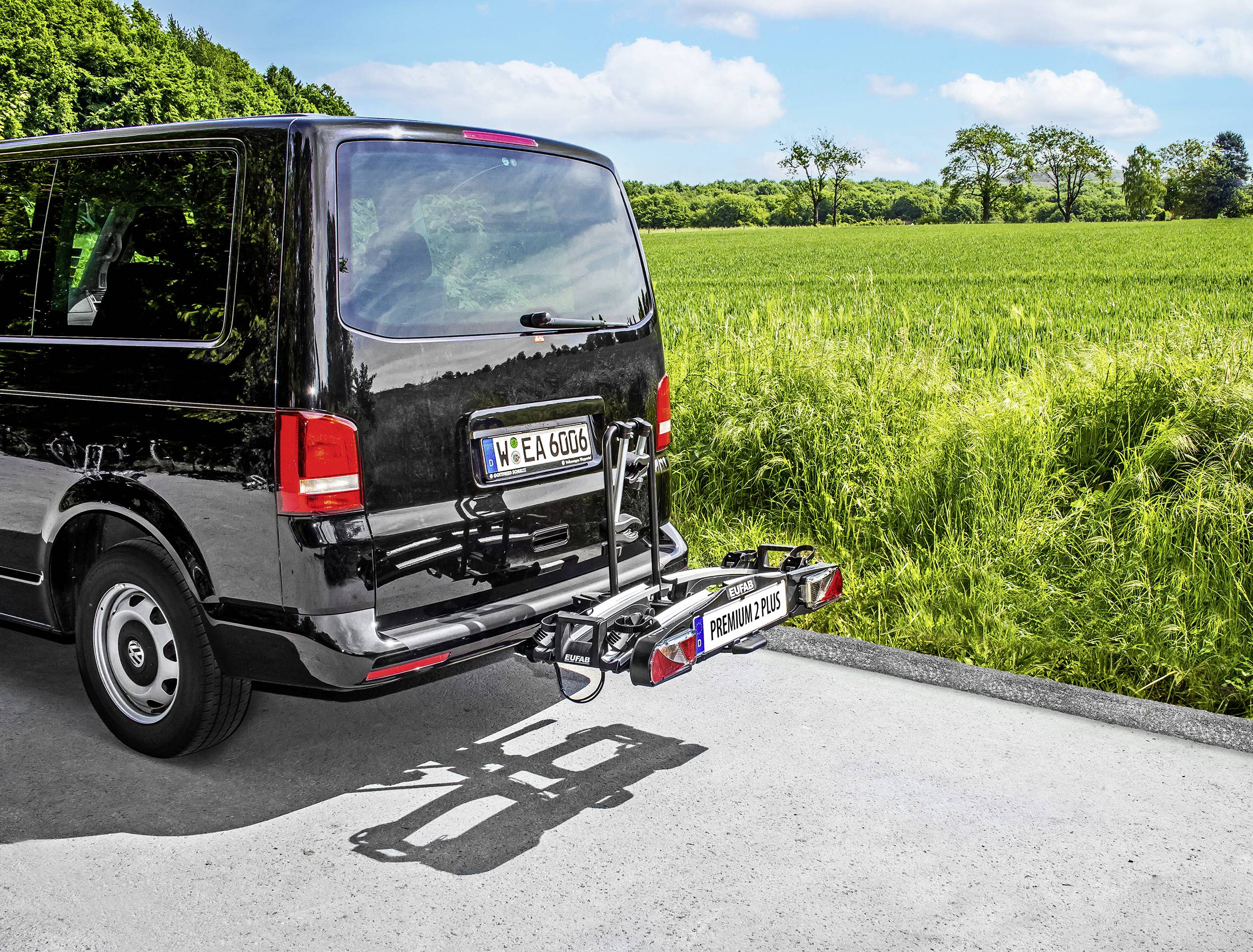 Czarny van z bagażnikiem rowerowym z tyłu stoi na drodze obok zielonej łąki pod niebieskim niebem.