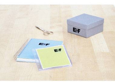 Niebieski notes, żółte etui na płytę CD, nożyczki i niebieskie pudełko z logo 'Elf' na drewnianym stole.