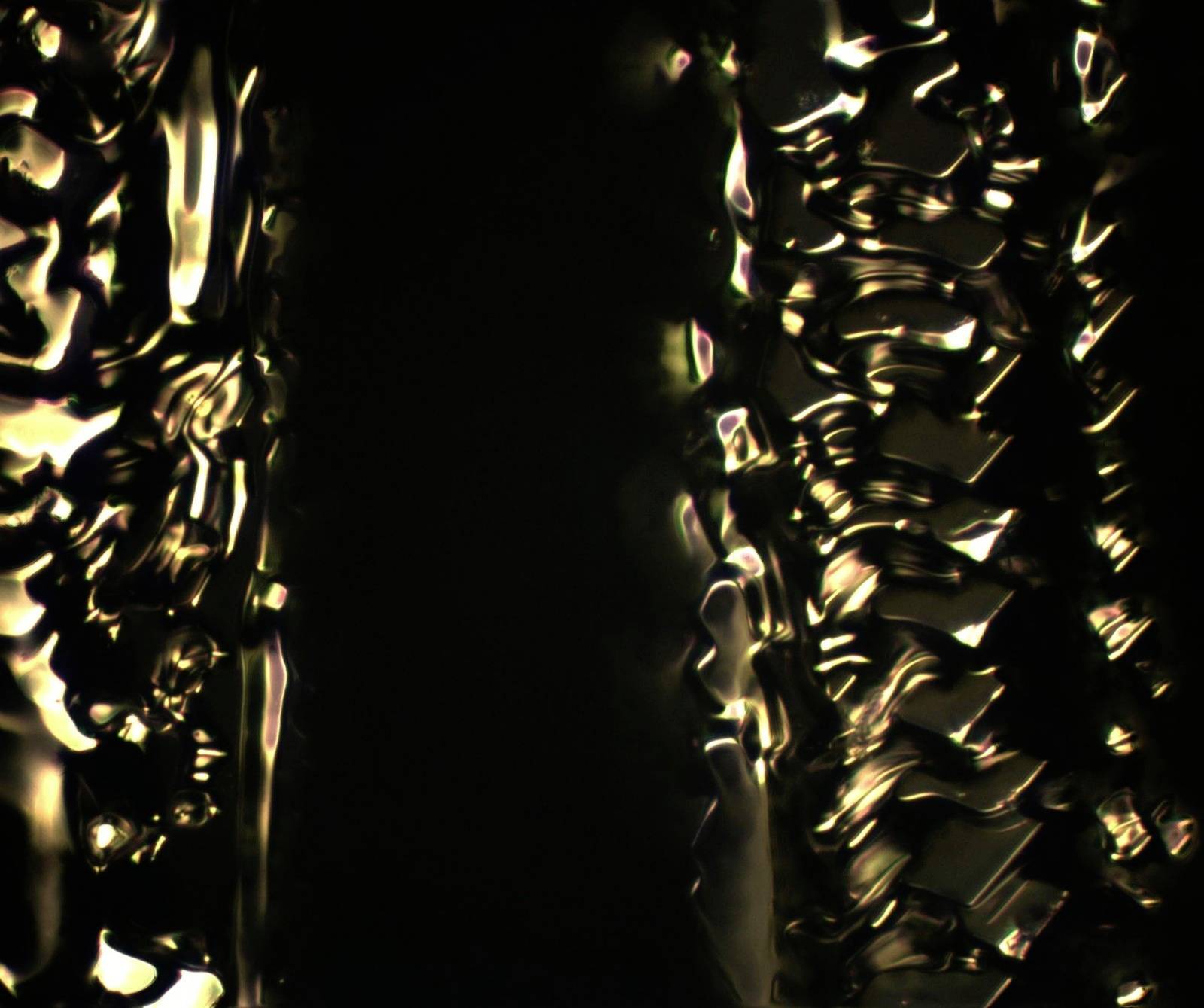 Abstrakcyjny, bliski kadr przedstawiający złote światło odbijające się na ciemnym tle, z falistymi liniami i fakturami.