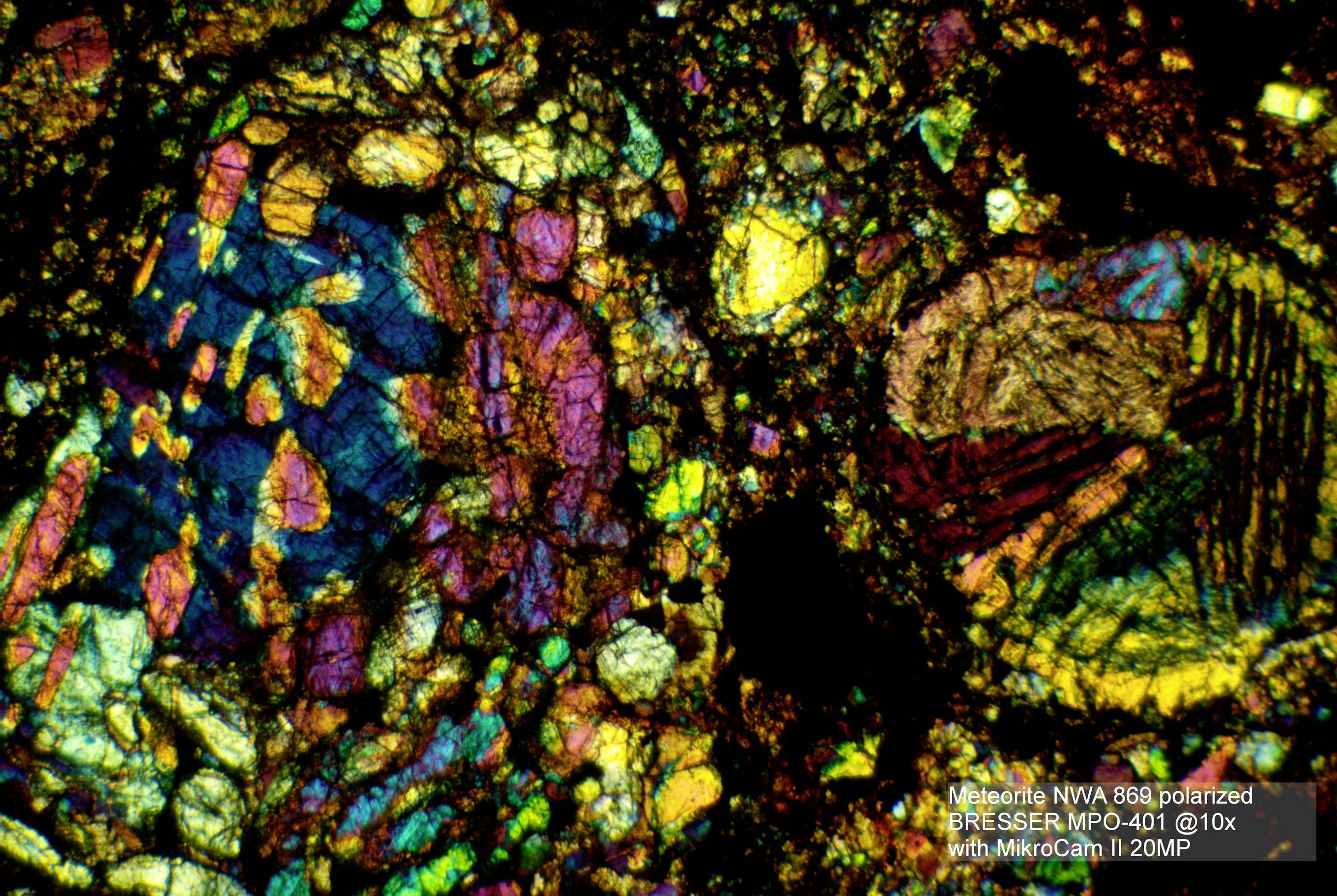 Obraz mikroskopowy fragmentu meteorytu ujawnia kolorowe, nieregularne wzory krystaliczne z różnymi strukturami mineralnymi.