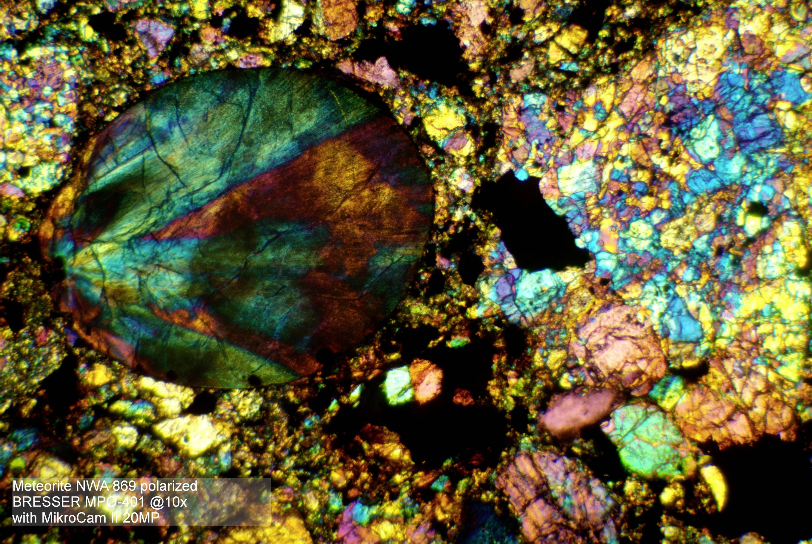 Kolorowy, mikroskopowy obraz meteorytu w świetle spolaryzowanym, ukazujący struktury krystaliczne i różnorodność mineralną.