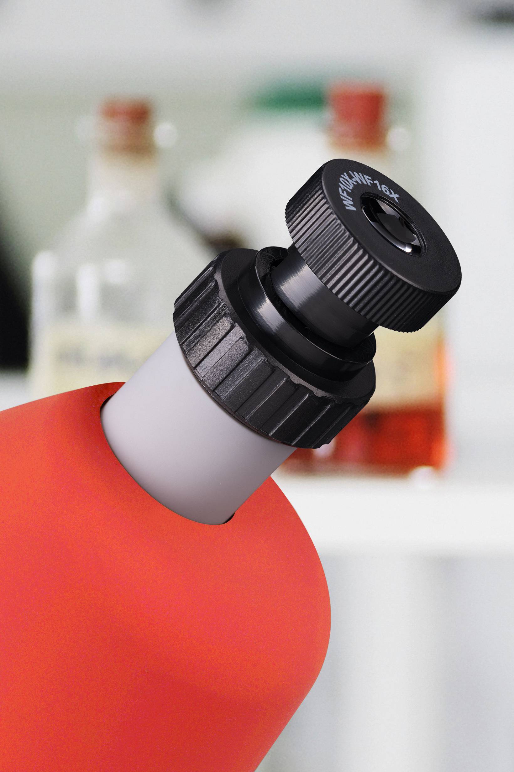 Mikroskopowa okular w zbliżeniu, w tle niewyraźnie widoczne są dwie butelki w laboratorium.