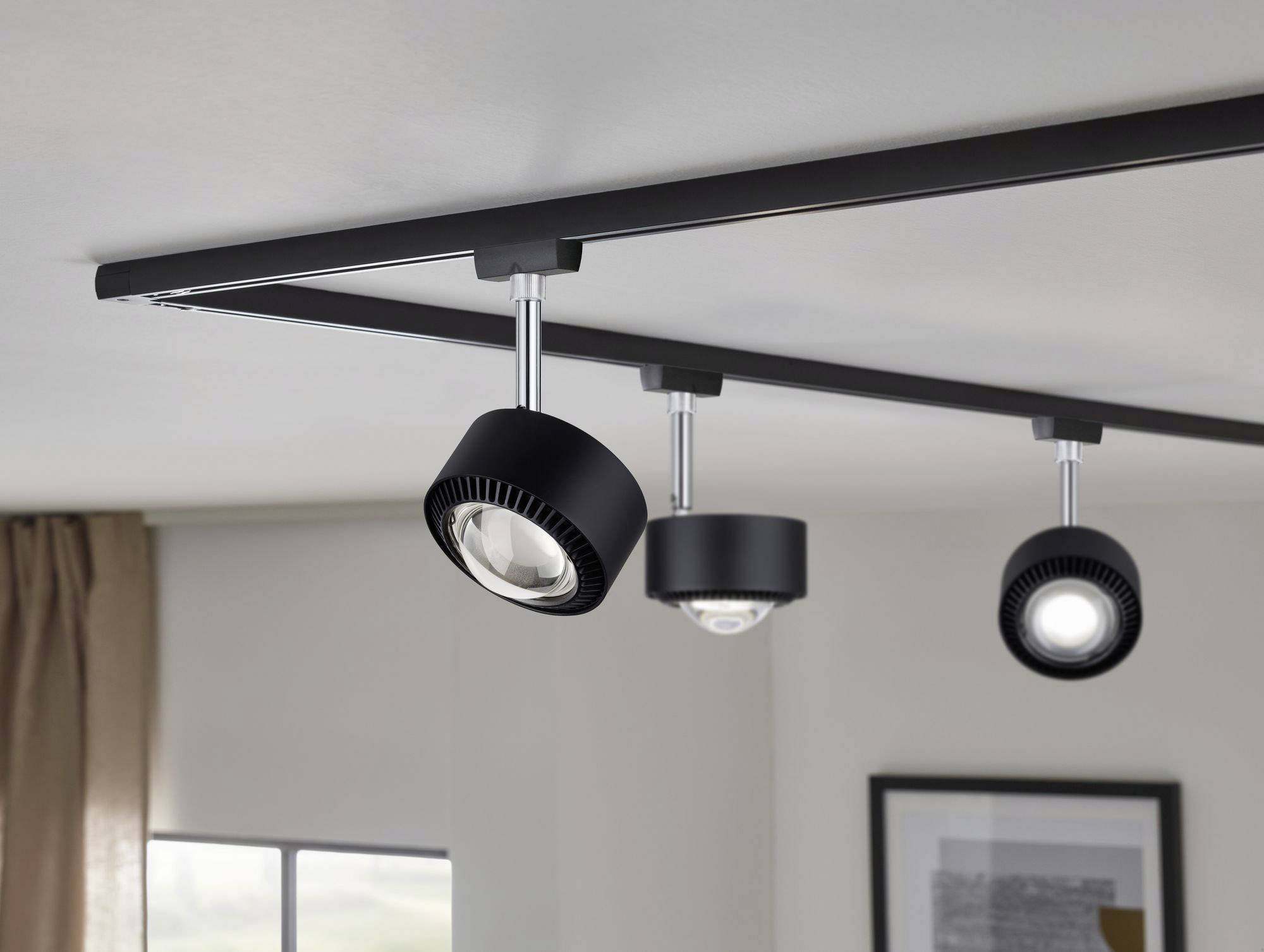 Trzy czarne reflektory sufitowe są zamontowane na szynie i świecą w różnych kierunkach. Znajdują się w nowoczesnym pomieszczeniu.
