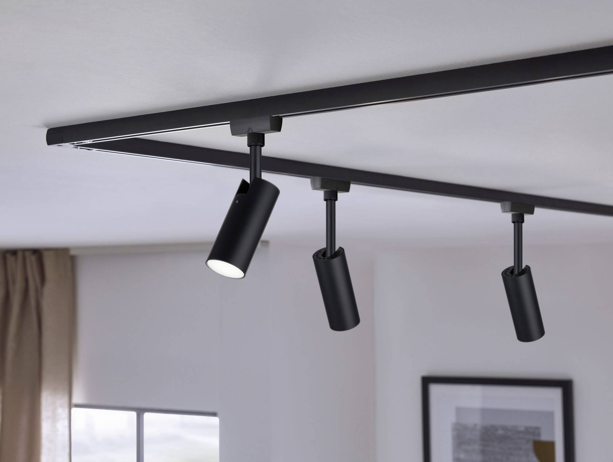 Trzy czarne reflektory sufitowe na szynie zamocowanej do sufitu, jeden z nich świeci w dół. Nowoczesne oświetlenie wnętrza.