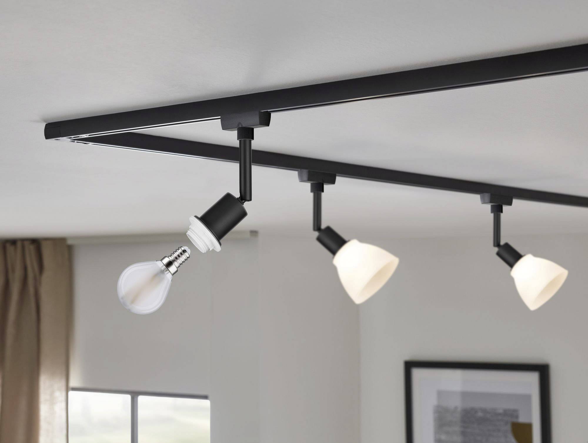 Trzy lampy sufitowe na szynie, dwie świecą się, jedna bez abażuru. W tle widoczne są okno i obraz na ścianie.