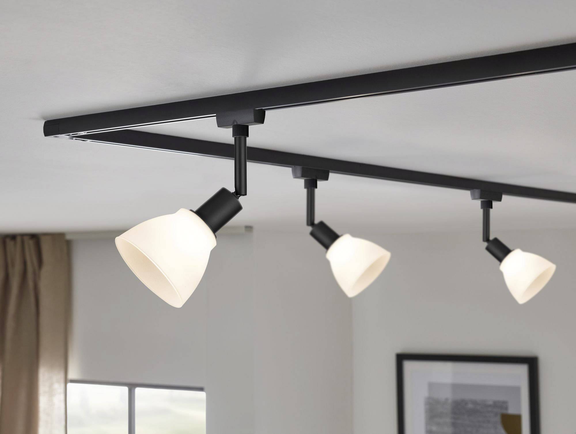 Trzy obrotowe lampy sufitowe z czarnymi uchwytami i białymi kloszami w nowoczesnym pokoju mieszkalnym.