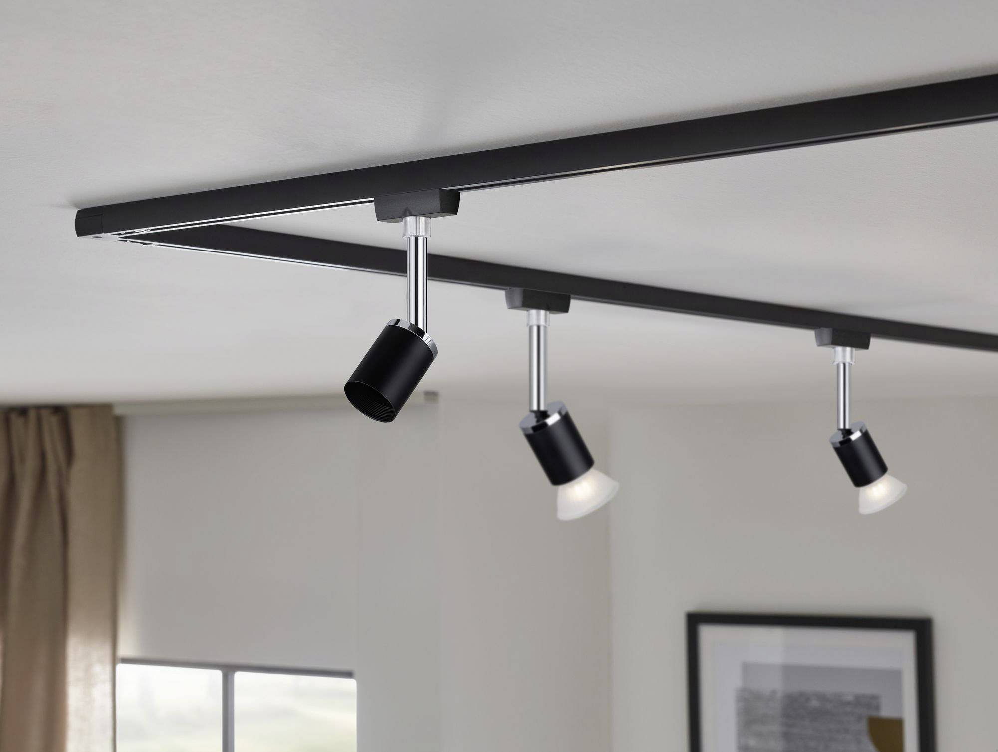 Czarna lampa sufitowa z trzema regulowanymi reflektorami w nowoczesnym salonie. W tle widać okno i obraz.