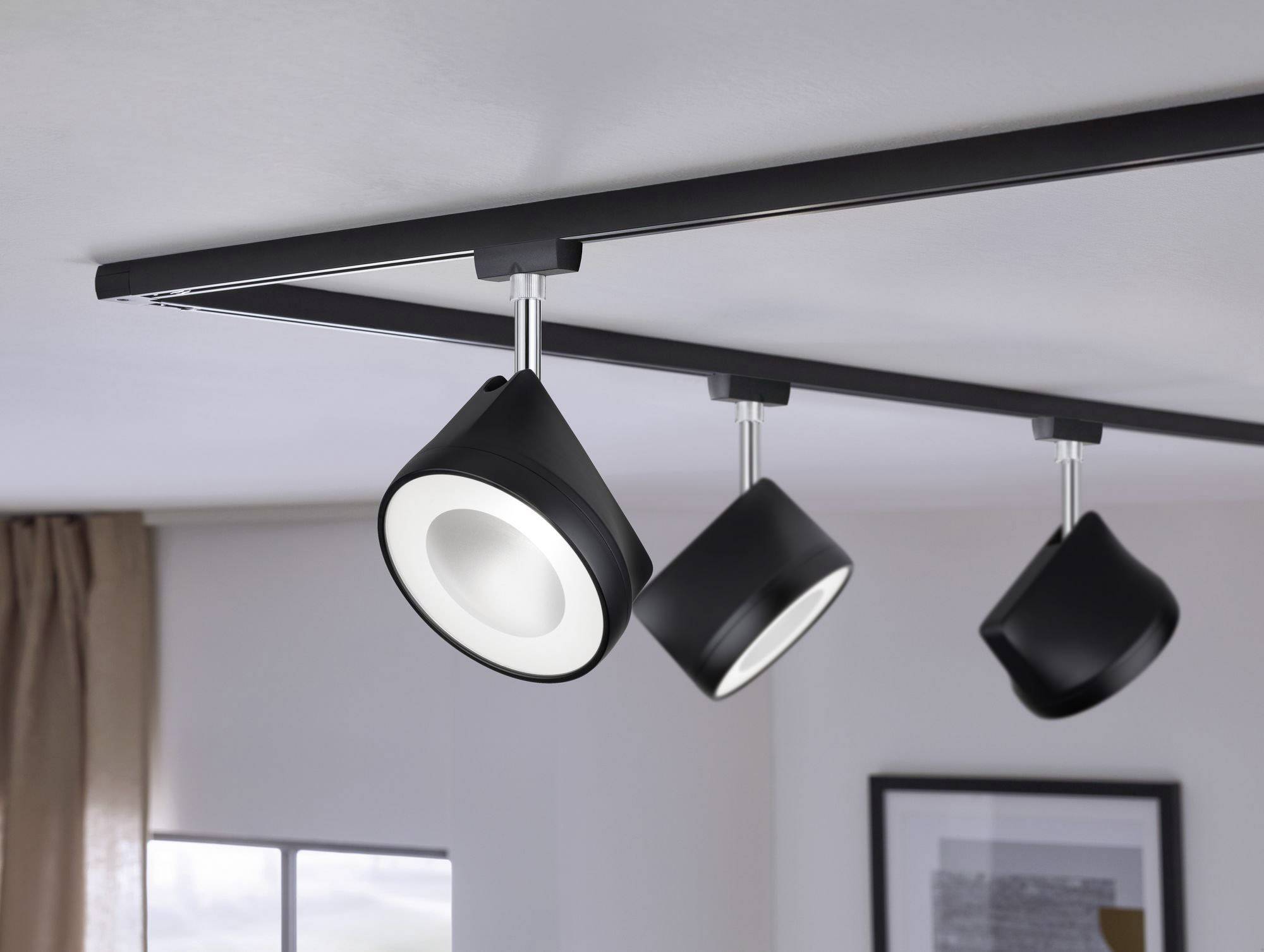 'Trzy czarne reflektory sufitowe na szynie w nowoczesnym pomieszczeniu, precyzyjnie oświetlające podłogę.'