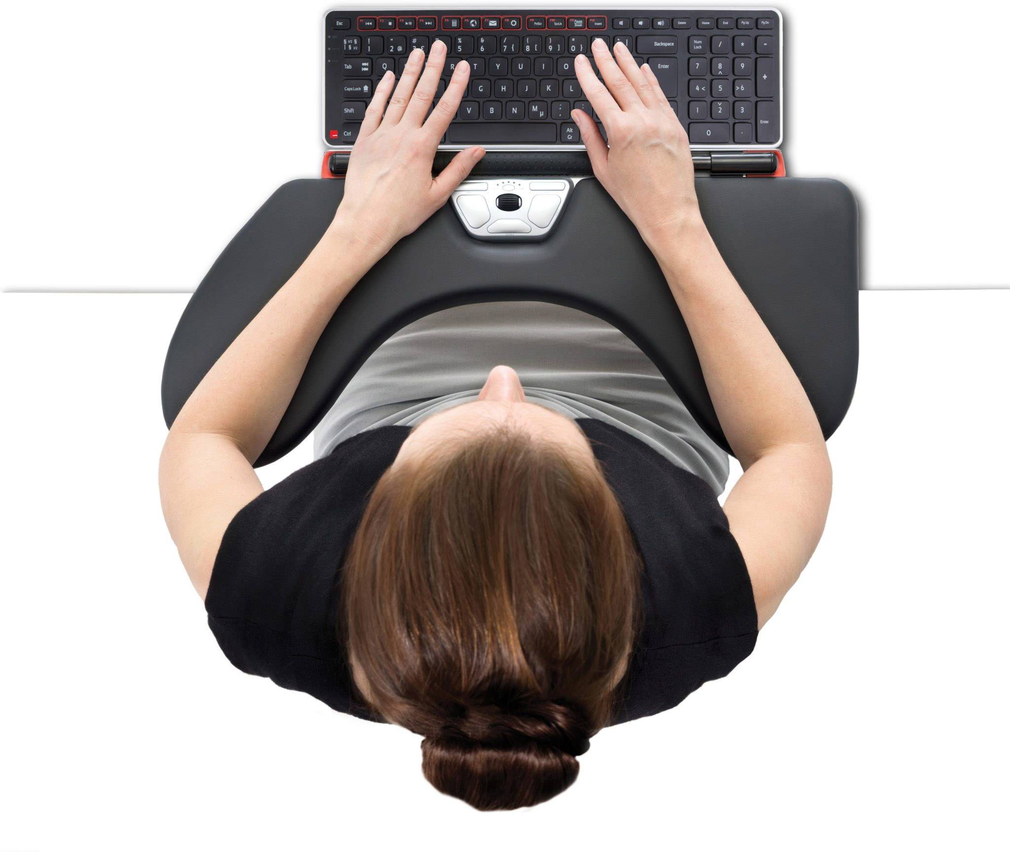 Kobieta stuka w czarną klawiaturę. Siedzi przy białym biurku, a jej brązowe włosy są związane w kok.