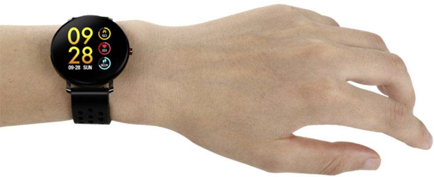 Dłoń trzyma czarny smartwatch z okrągłą tarczą. Na zegarku widać godzinę '09:28'.