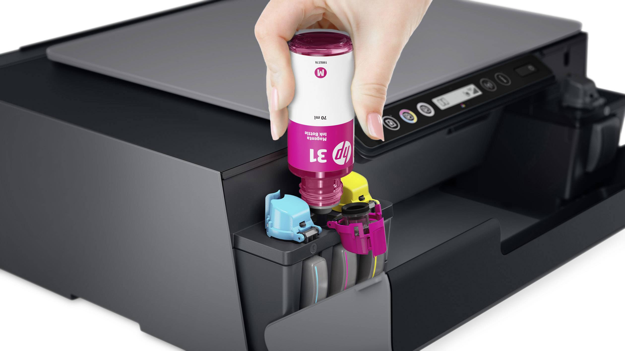 Ręka napełnia drukarkę tuszem magentowym, po lewej stronie widoczne są żółte i niebieskie kartridże, przed drukarką.