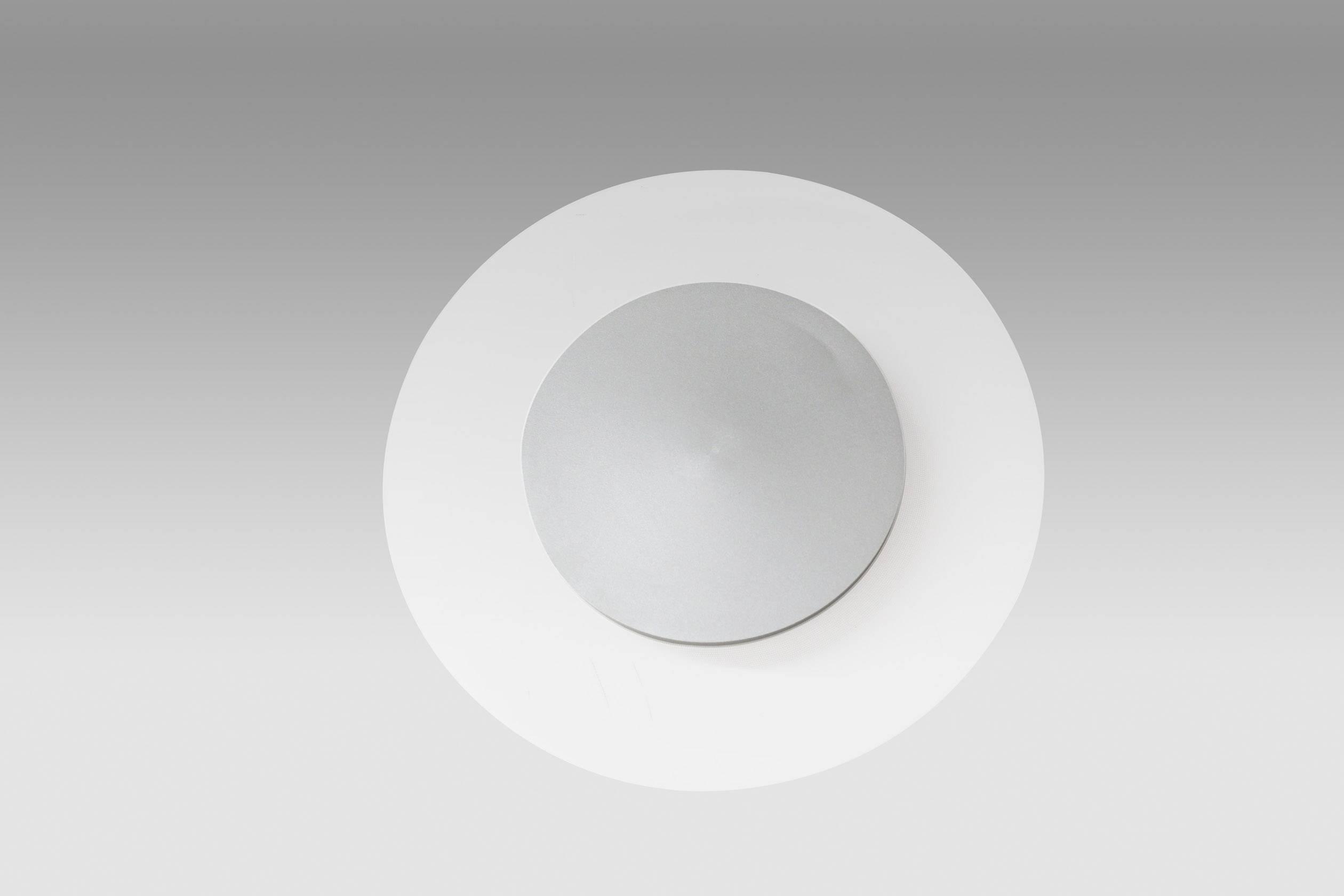 Okrągła, srebrna płyta metalowa na jasnoszarym tle.