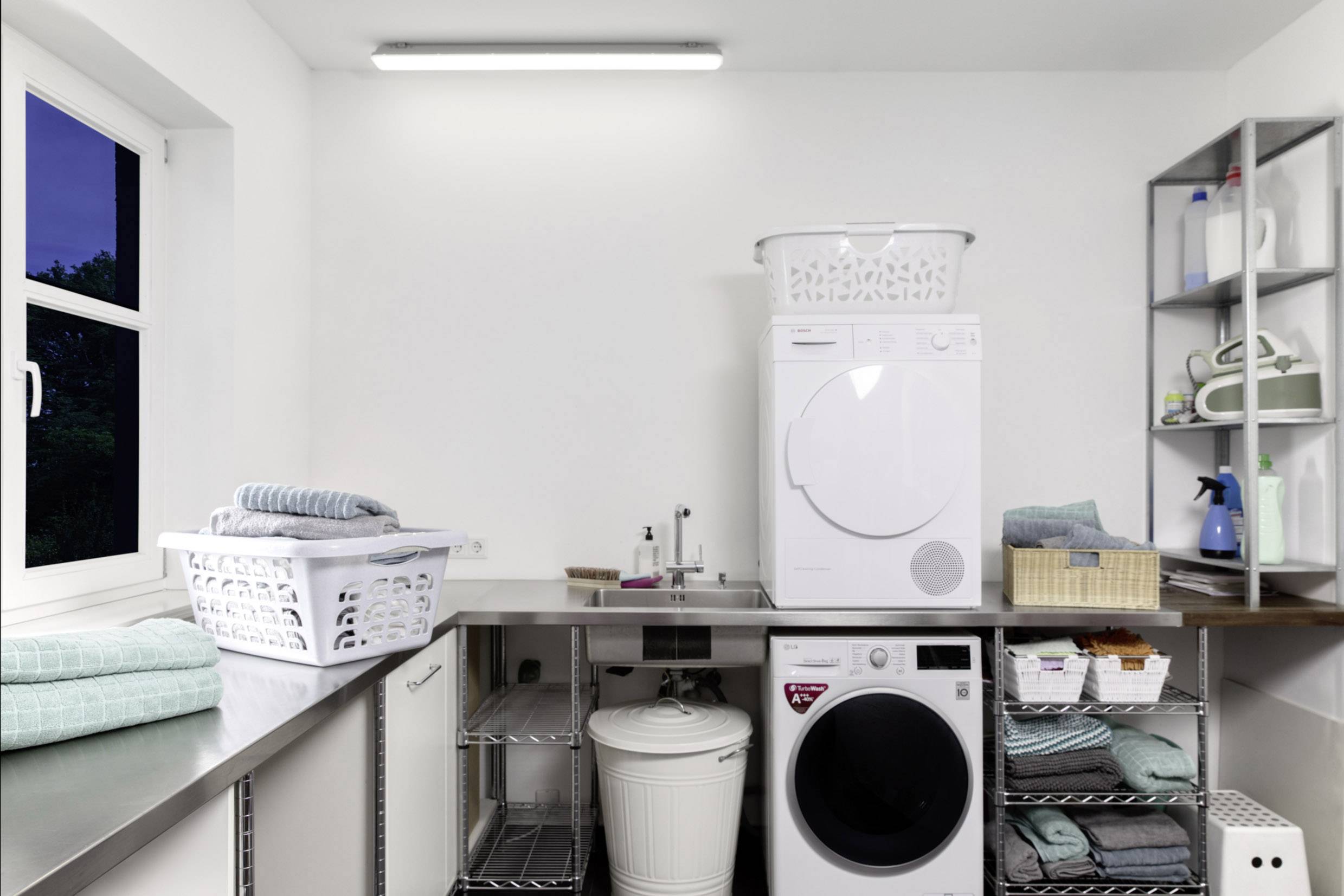 Pralnia z pralką, suszarką, półkami i koszami. Uporządkowane i dobrze zorganizowane pomieszczenie z naturalnym światłem dziennym wpadającym przez okno.