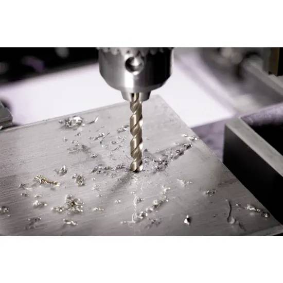 Wiertło wykonuje otwór w metalowej powierzchni, wokół którego rozrzucone są wióry metalowe, co wskazuje na proces produkcyjny lub budowlany.