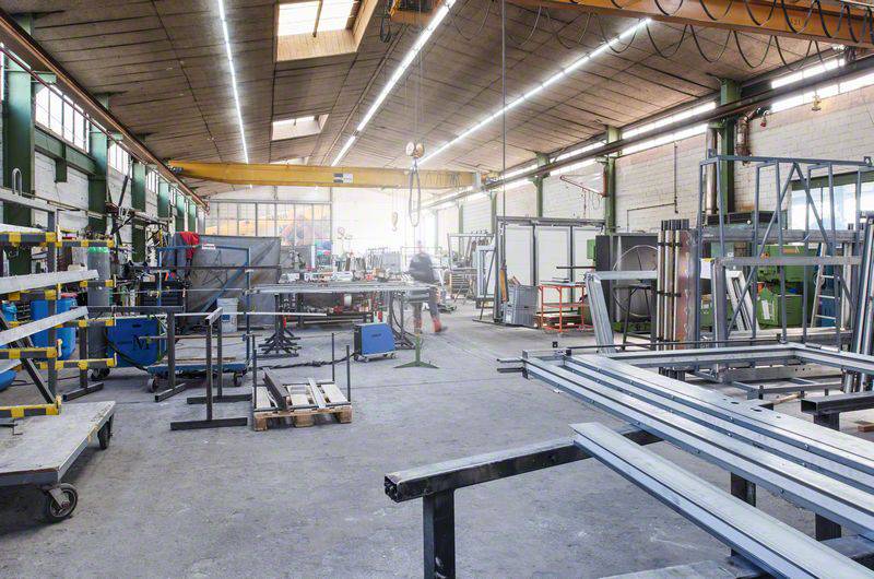 Duża metalowa pracownia z narzędziami, stanowiskami roboczymi i maszynami. W tle jedna osoba pracuje przy maszynie.