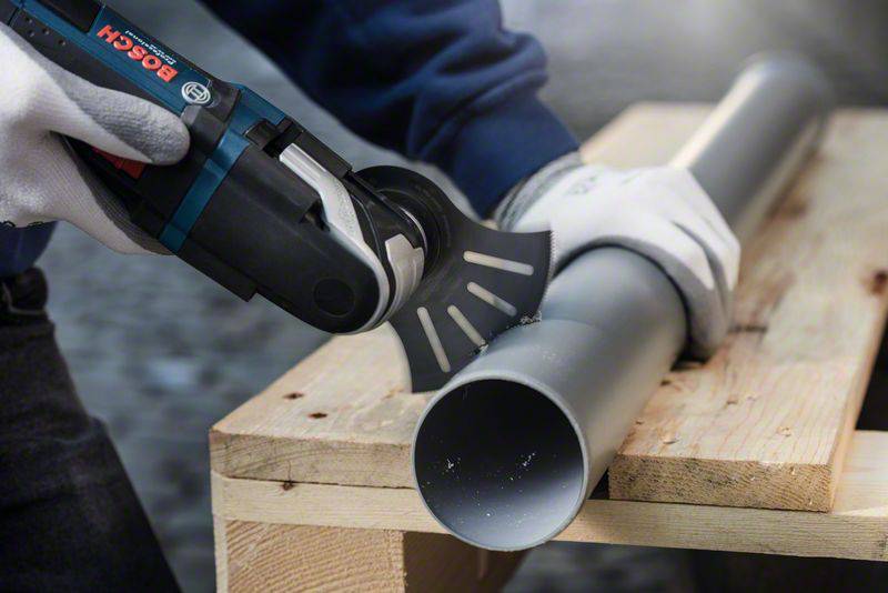 Osoba przecina rurę plastikową elektronarzędziem wielofunkcyjnym na drewnianym stole. Nosi rękawice ochronne dla bezpieczeństwa.