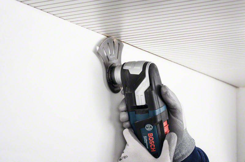 Osoba trzyma elektronarzędzie marki Bosch i przycina krawędź sufitu. Rękawice chronią dłonie podczas cięcia.