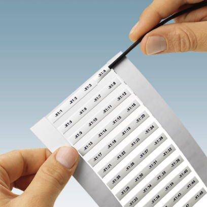 Dwie ręce trzymają arkusz z ponumerowanymi naklejkami. Etykiety przedstawiają kolejne numery od #111 do #122.