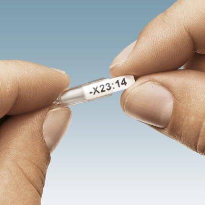 Dwie ręce trzymają małą przezroczystą kapsułkę z etykietą oznaczoną napisem '-X23:14'. Tło w kolorze niebieskim.