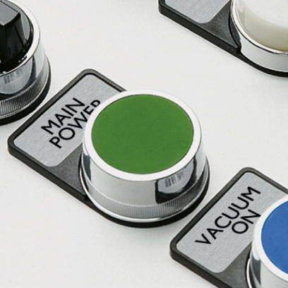 Trzy elementy kontrolne z etykietami 'GŁÓWNE ZASILANIE', 'PRÓŻNIA WŁ.' oraz zielony przycisk pośrodku. Sterują one funkcjami.