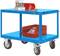 Niebieski wózek warsztatowy na czterech kołach, na którym znajduje się czerwone pudło plastikowe, bloki metalowe i narzędzia. Idealny do przechowywania narzędzi.
