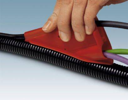 Dłoń zamyka czerwoną osłonę kabli wokół kilku przewodów oraz czarny kanał kablowy, aby je zorganizować i zabezpieczyć.