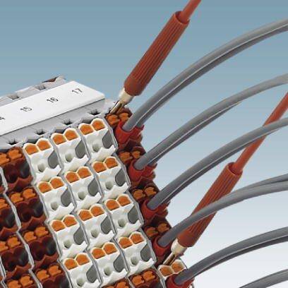 Na elektrycznej listwie zaciskowej podłączonych jest kilka przewodów w kolorach pomarańczowym i szarym. Zaciski są rozmieszczone w rzędach.