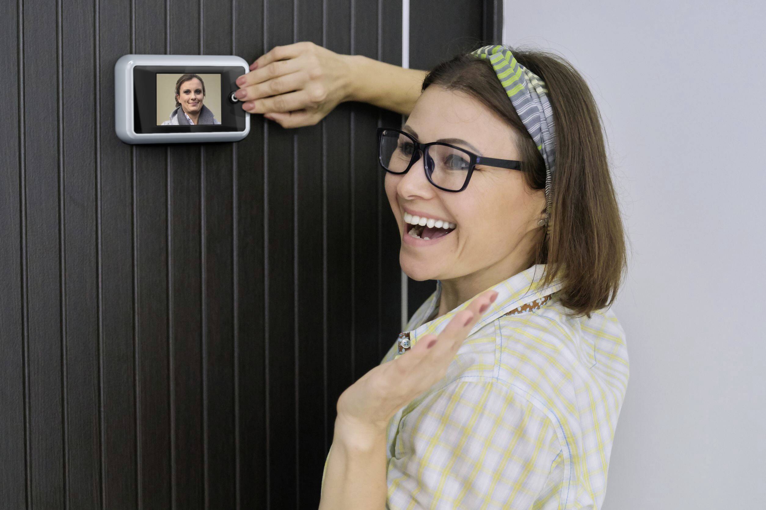 Kobieta w kraciastej koszuli uśmiecha się, patrząc na ekran z wideorozmową, dotykając ręką ekranu.